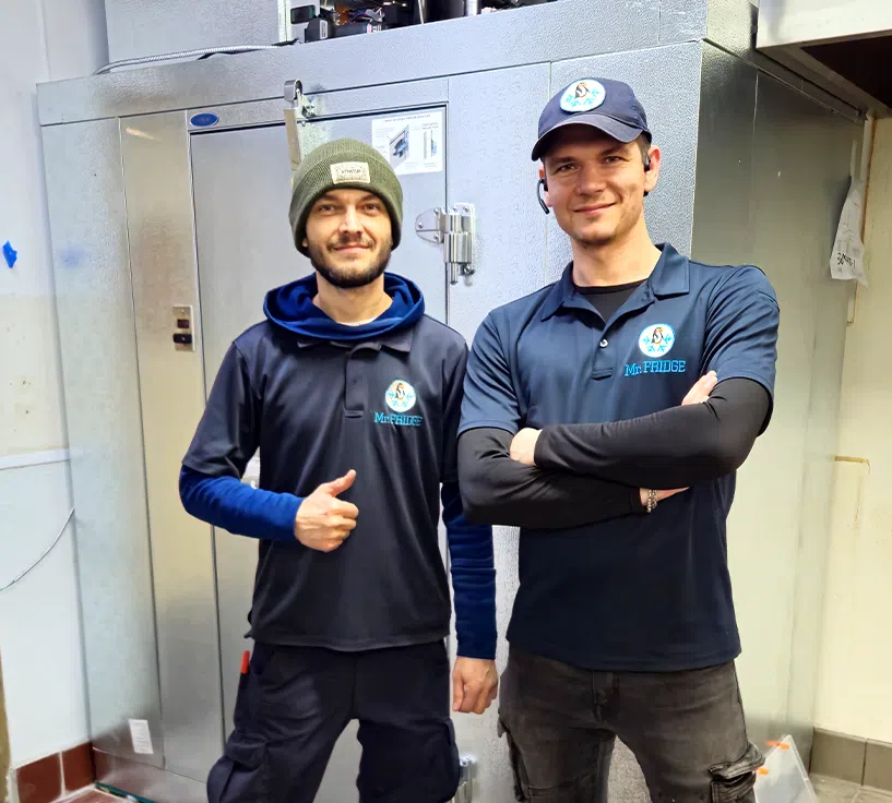 Two Mr. Fridge technicians standing in front of a repaired walk-in cooler after completing service.