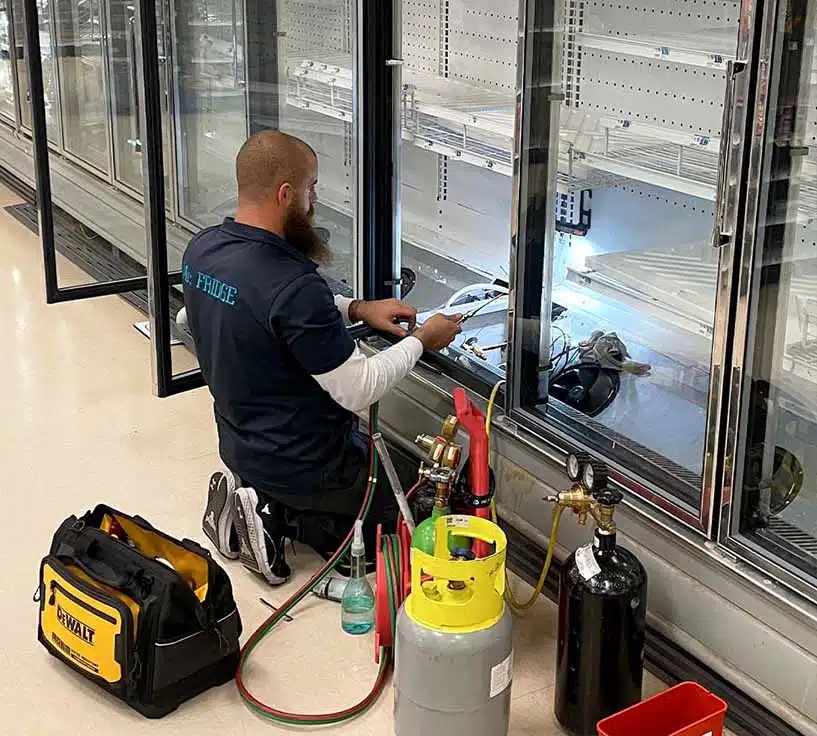 Mr. Fridge Display Fridge Repair Service - Seattle WA Mr. Fridge technician repairing a commercial glass door display refrigerator with diagnostic tools in Seattle, WA.